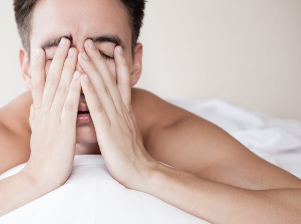 man holding tired face on bed