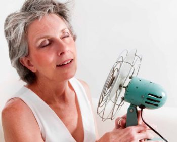 middle aged woman holding fan to cool down